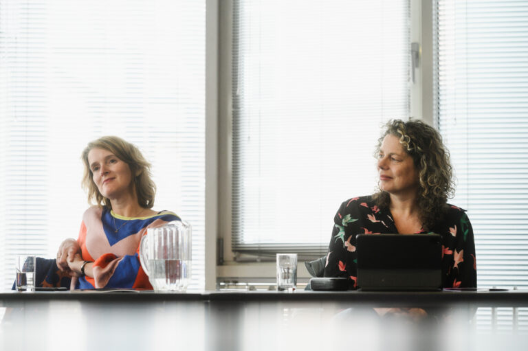 twee vrouwen zitten aan een tafel in een luisterhouding
