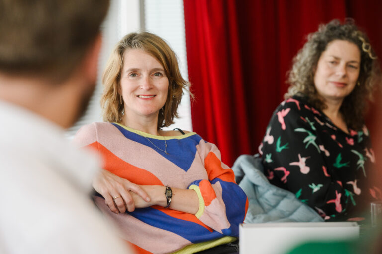 Vrouw in felgekleurde trui leunt op de stoel en lacht