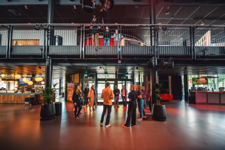 Groep mensen staat in een modern interieur met meerdere niveaus en planten.