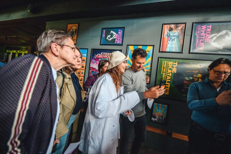 Een groep mensen kijkt en praat tijdens een bezoek aan een kunsttentoonstelling, omringd door kleurrijke posters aan de wand.