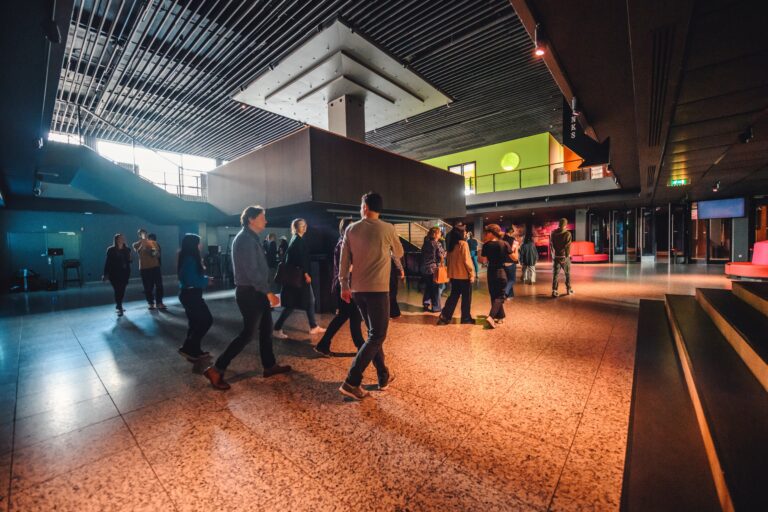 Een drukke lobby met mensen die zich bewegen in een modern, architectonisch interieur.