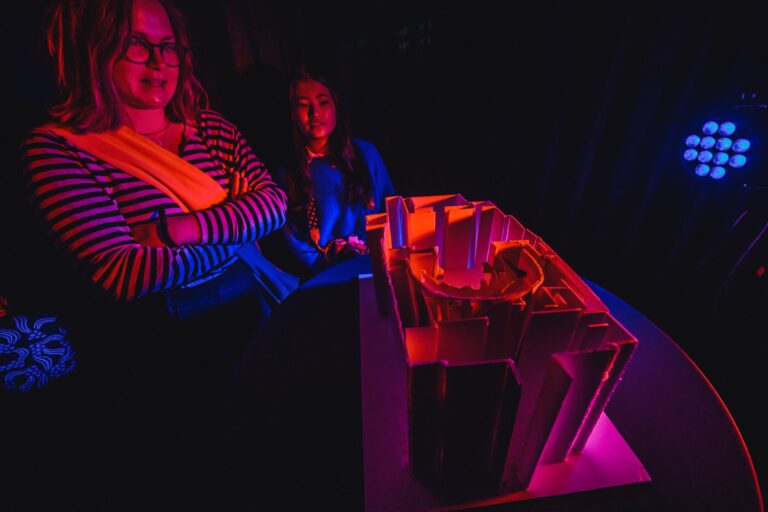 Twee meisjes zitten naast een tafel met een helder verlichte object in neonkleuren.
