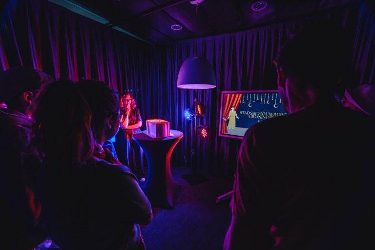 Mensen in een verduisterde ruimte met paarse en blauwe verlichting, kijken naar een scherm.