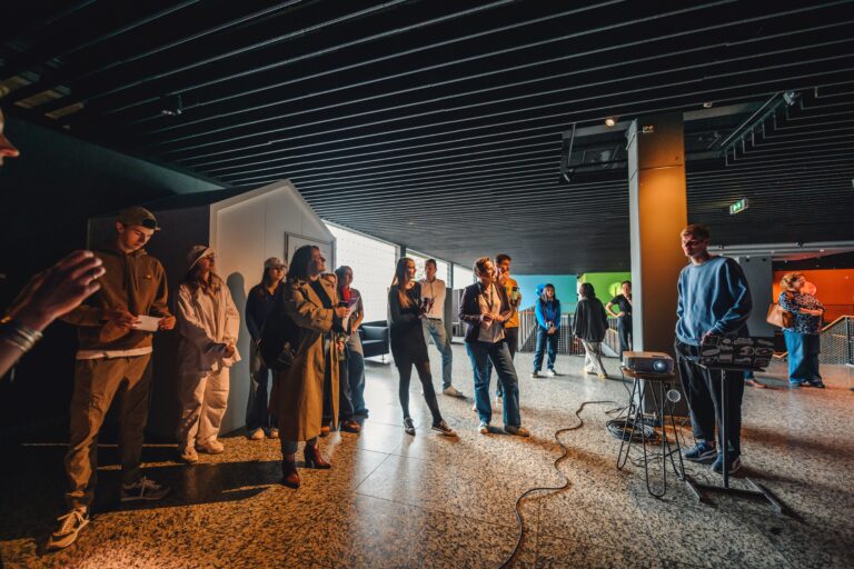 Een groep mensen staat in een moderne ruimte rond een persoon die een presentatie houdt.