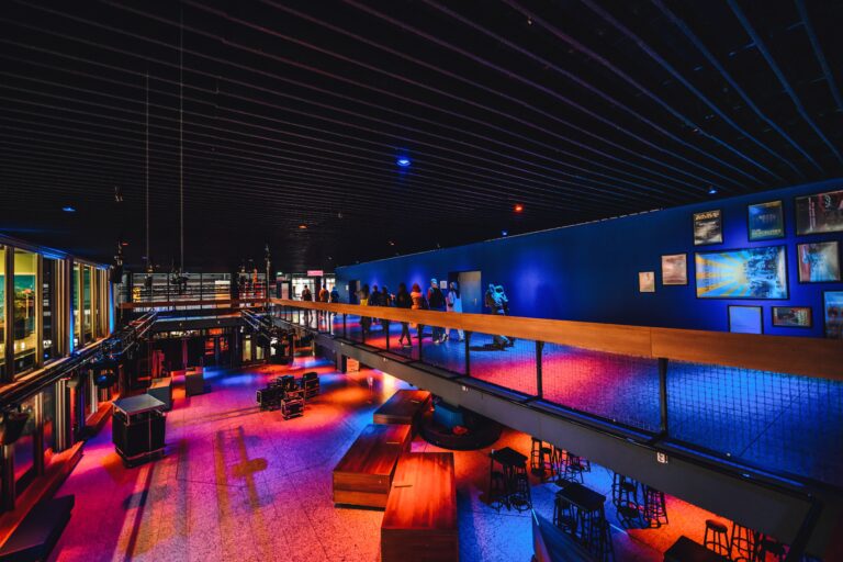 Een moderne lounge met kleurrijke verlichting en zitgedeelten, gezien vanaf een verhoogd platform.