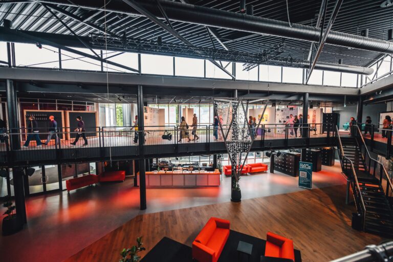 Moderne kantoorruimte met hoge plafonds, een bovenste loopbrug, en rode meubels.