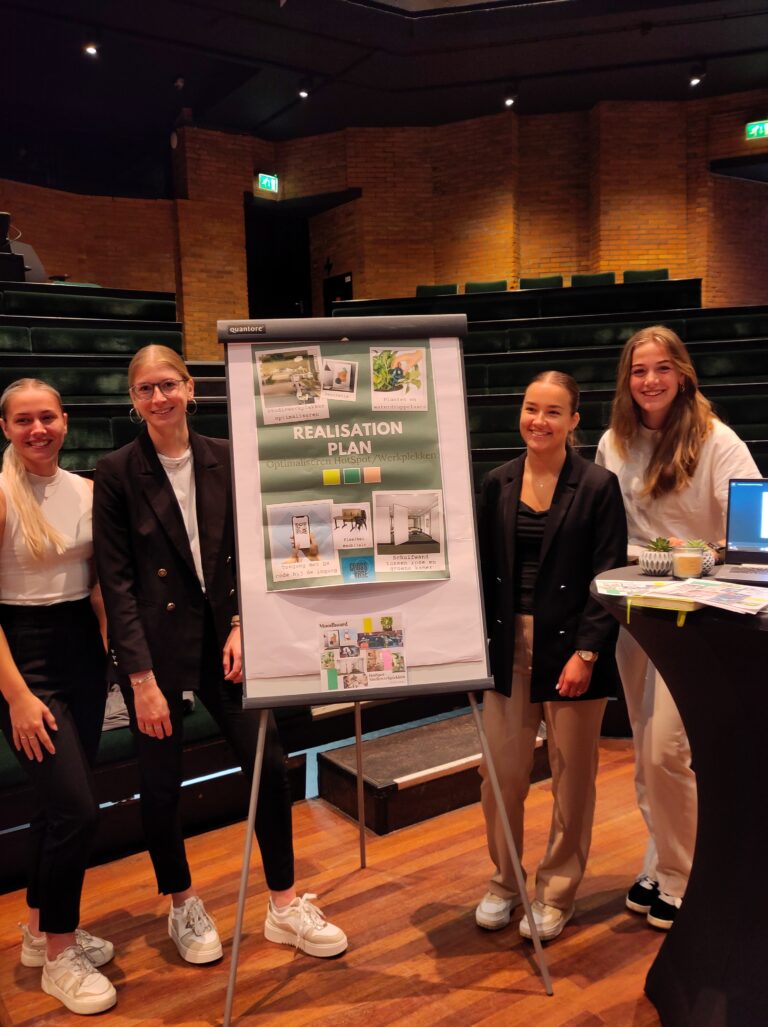 Vier mensen staan naast een presentatiebord in een auditorium.