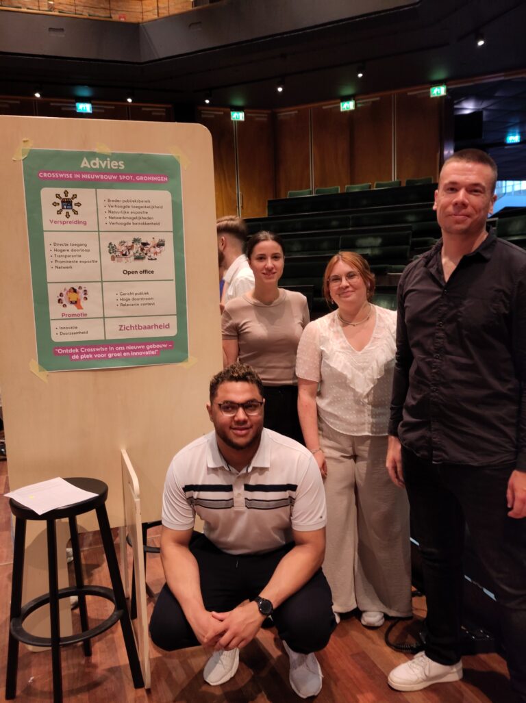 Vier mensen poseren voor een presentatiebord in een auditorium.