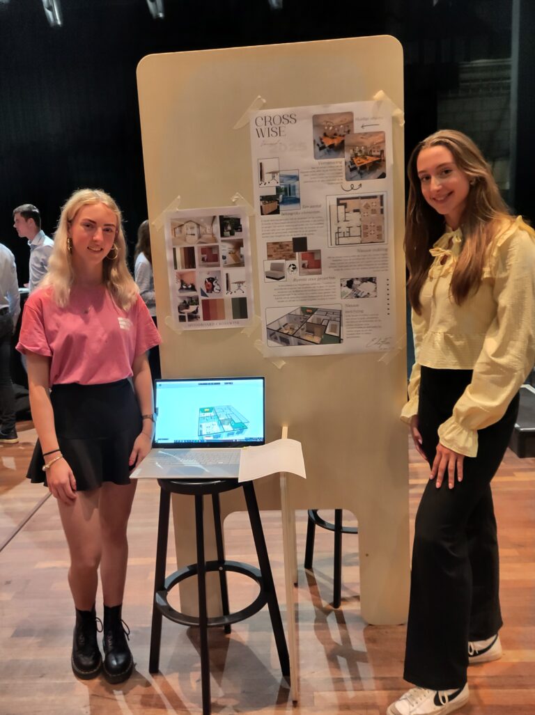 Twee vrouwen staan naast een presentatiebord met afbeeldingen en een laptop op een tafel.