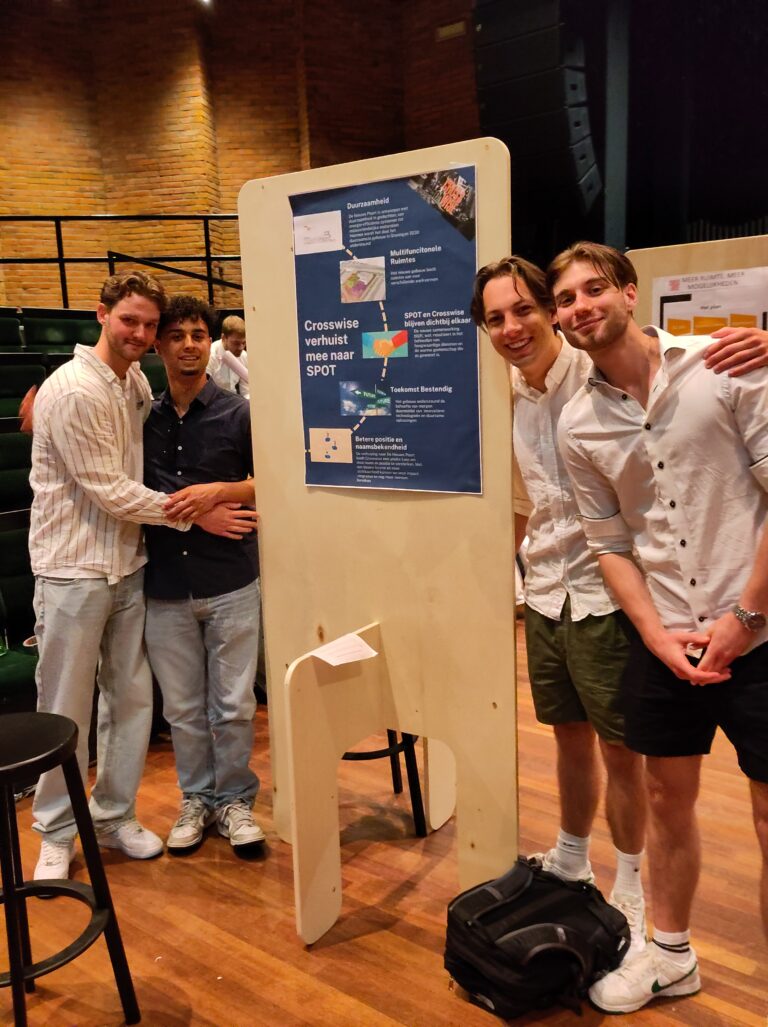 Vier lachende mannen poseren bij hun presentatiebord op een evenement.