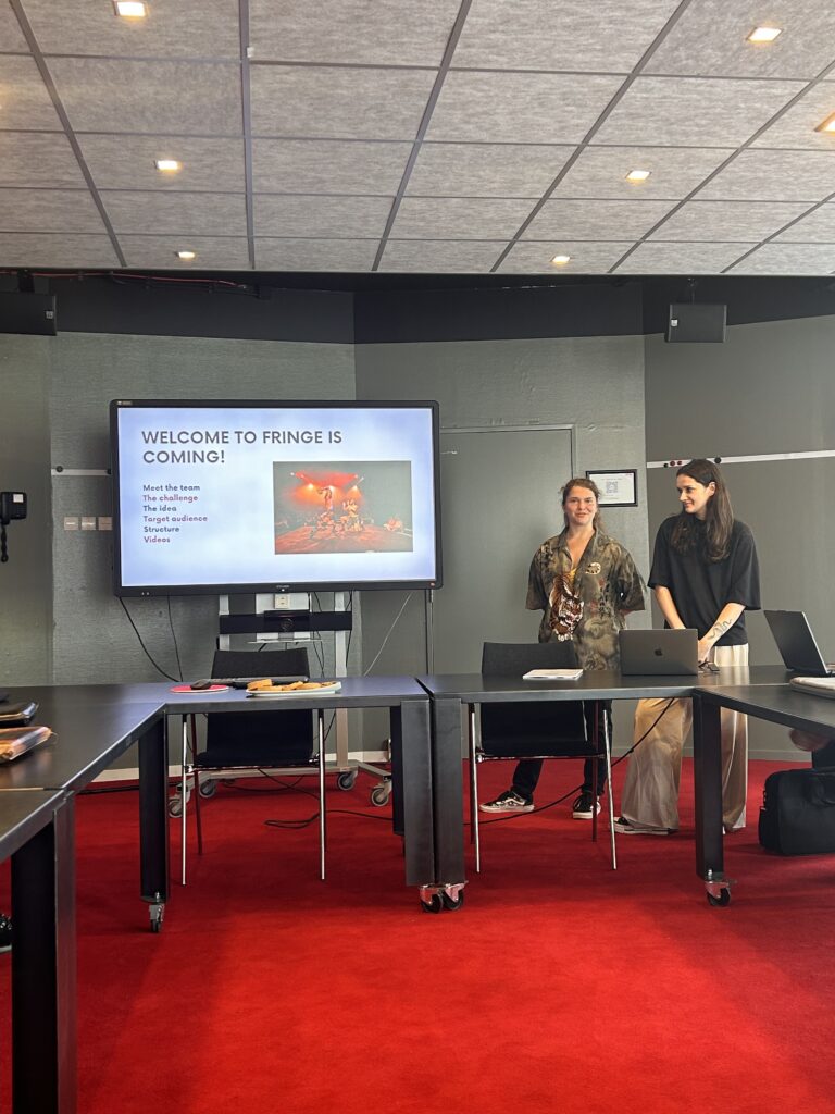 twee meiden geven hun presentatie over fringe en staan voorin de zaal