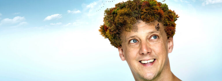 Het hoofd van Jochem Myjer met als achtergrond een blauwe lucht. Als je inzoomt op het hoofd van Jochem zie je dat zijn haar een bos is en dat er dieren rondlopen.