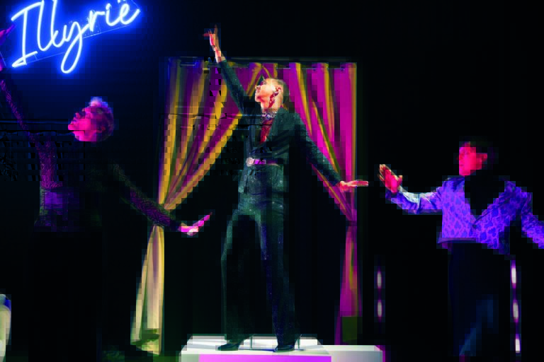 Drie personen in glitterkleding staan op het podium te dansen