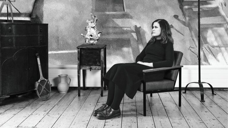 Zwart geklede vrouw zit op stoel in huiskamer en staart in de verte