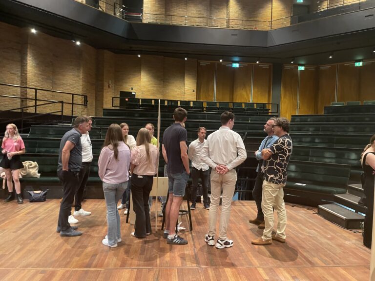 Een groep mensen staat in een kring op een toneel in een theater.