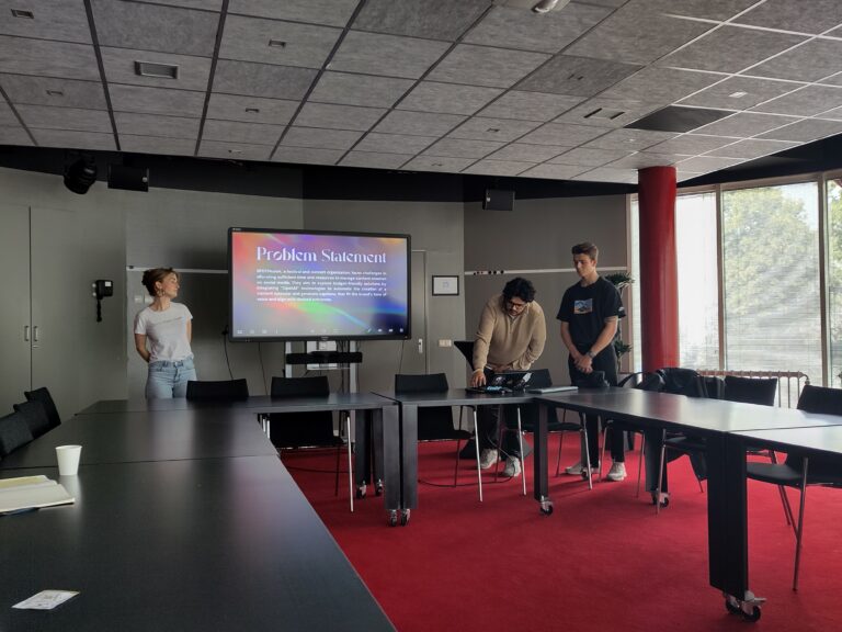 Drie personen geven een presentatie in een vergaderruimte met een groot scherm op de achtergrond.