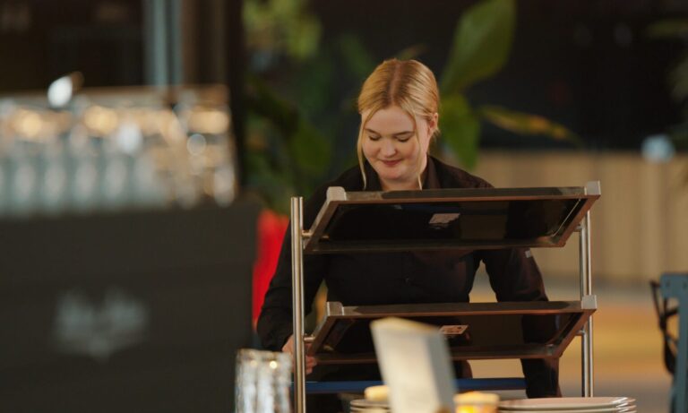 Een vrouw met een blonde paardenstaart werkt bij een balie in een restaurant.