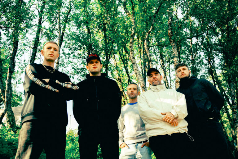 Een groep van vijf mensen staat buiten voor bomen.