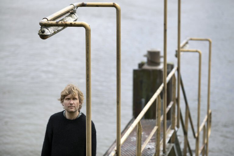 AWKWARD i, oftewel Djurre op een portret foto. Hij staat op een steiger wat hoort bij de zeevaart en in de achtergrond is de zee te zien.