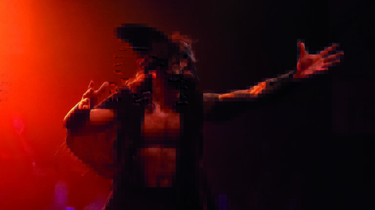 Een gepixeleerd beeld van een persoon die een optreden geeft met rode en donkere verlichting.