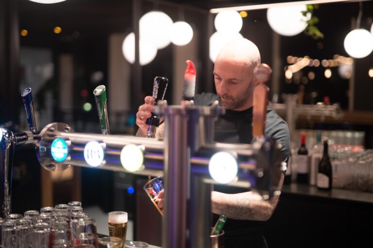 man tapt biertje achter de bar