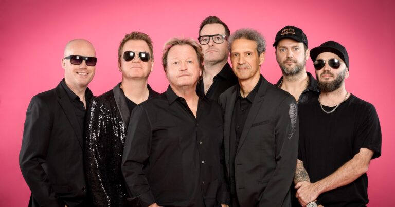 Een groepsfoto van de band Level 42 met een opvallend roze achtergrond.