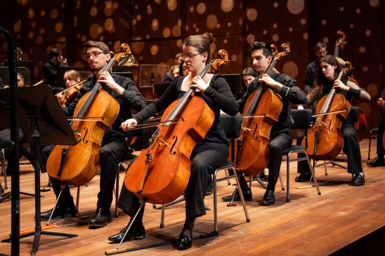 Op de voorgrond drie cellisten van he cello-ensemble van het PCC. OP de achtergrond publiek