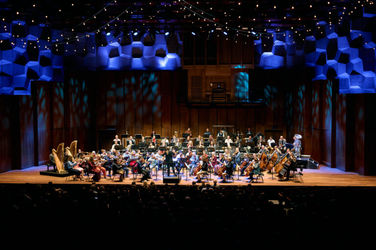 Orkest dat op een groot podium aan het spelen is met een volle zaal