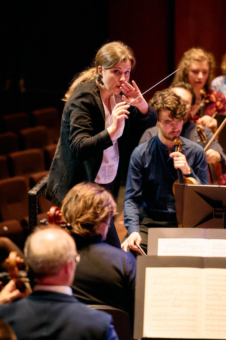 Vrouwelijk dirigent die aan het dirigeren is voor een orkest