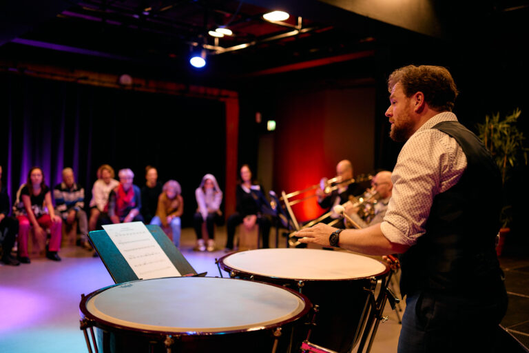 man die bij twee grote trommels staat en aan het vertellen is tegenover een groep mensen