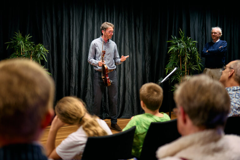 Orkest lid (viool) die wat aan het vertellen is tegen een groep mensen