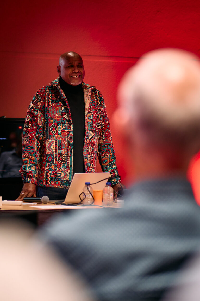 lachende man met een kleurrijk jasje die aan het vertellen is voor een groep mensen