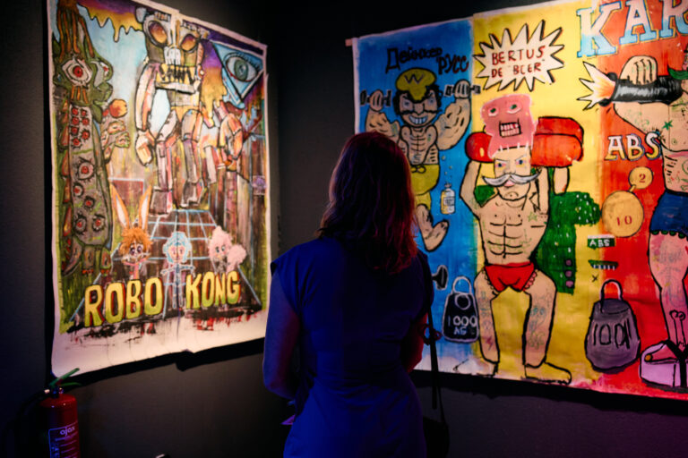 vrouw die aan het kijken is naar twee kunstwerken die aan de muur hangen