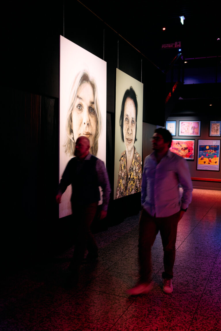twee mannen die langs een tentoonstelling lopen van portretten