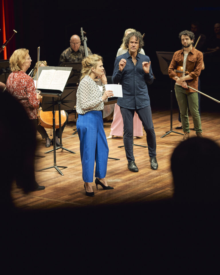 Jet Berkhout op het podium van de kleine zaal die een lezing geeft. Ze draagt een knalblauwe broek