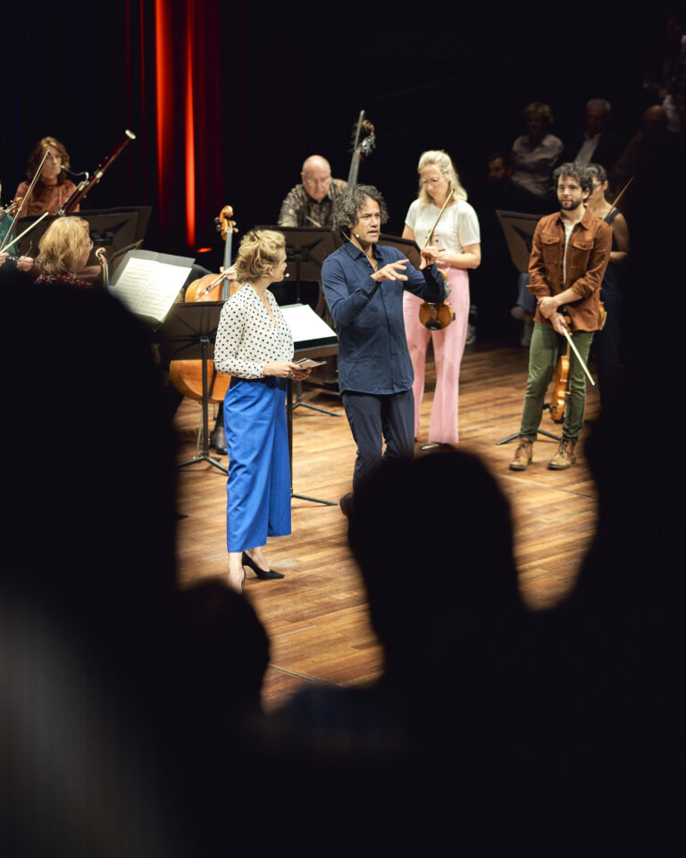 Jet Berkhout op het podium van de kleine zaal die een lezing geeft. Ze draagt een knalblauwe broek