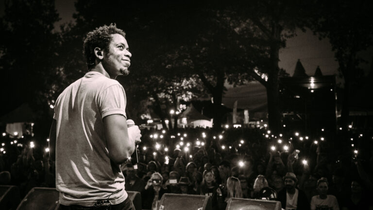 Een zwart-wit foto van rapper Typhoon, op een podium kijkend naar een groot publiek tijdens een live optreden, met vele lichten op de achtergrond.