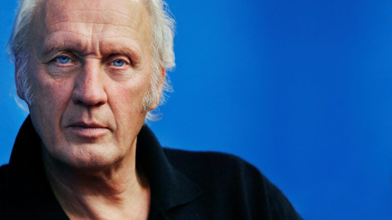 Foto van Herman van Veen met een blauwe achtergrond.