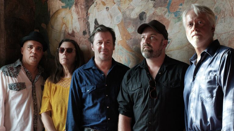 Een groep met mannen en een vrouw die poseren voor de camera voor een kleurrijke muur