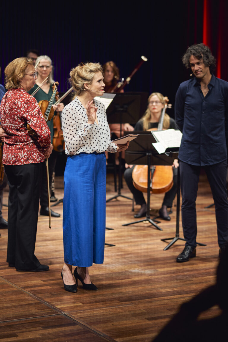 Jet Berkhout op het podium van de kleine zaal die een lezing geeft. Ze draagt een knalblauwe broek