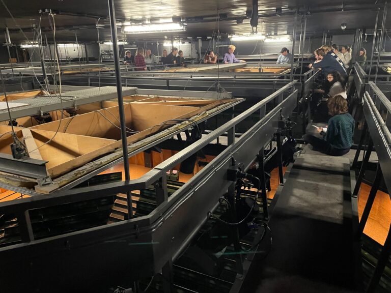 Een industriële ruimte met meerdere niveaus, waar mensen zich verspreid bewegen tussen metalen structuren en platforms.