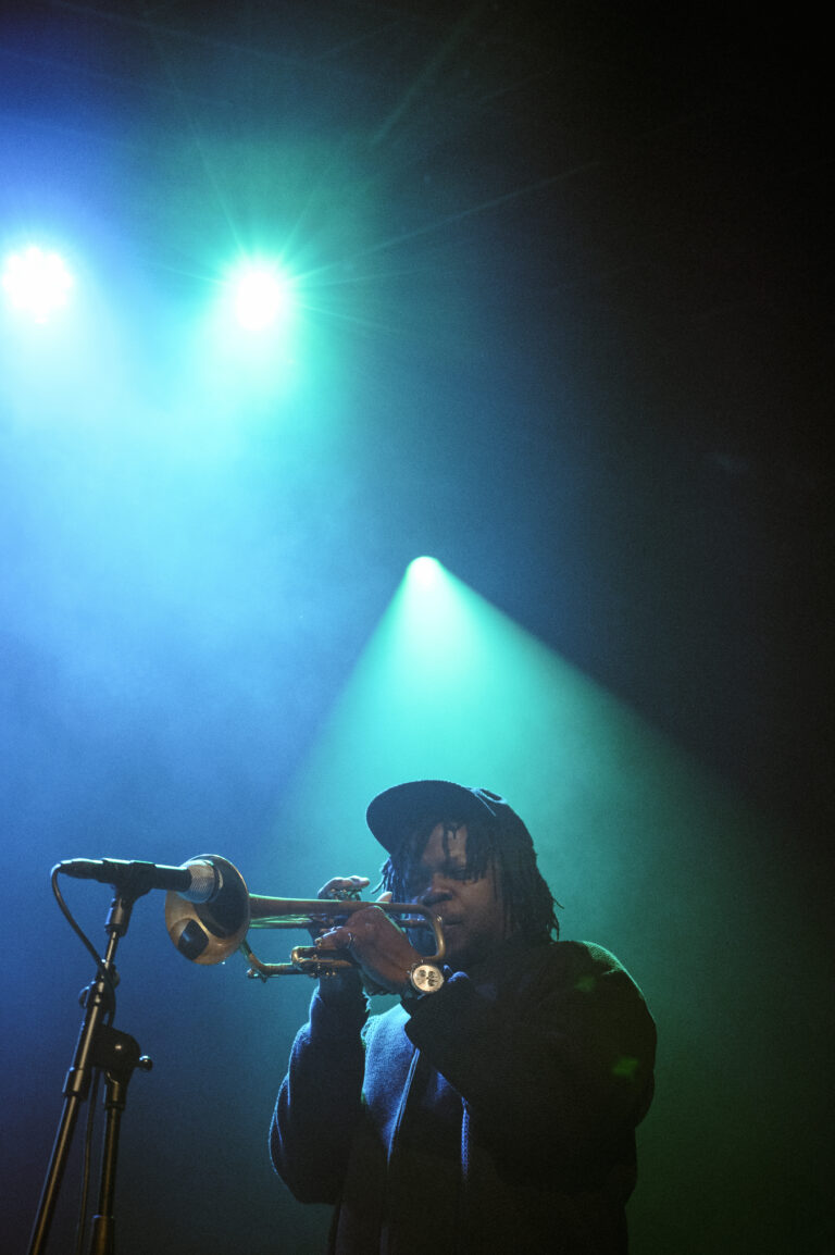 Een muzikant speelt trompet op een podium met kleurrijke verlichting.