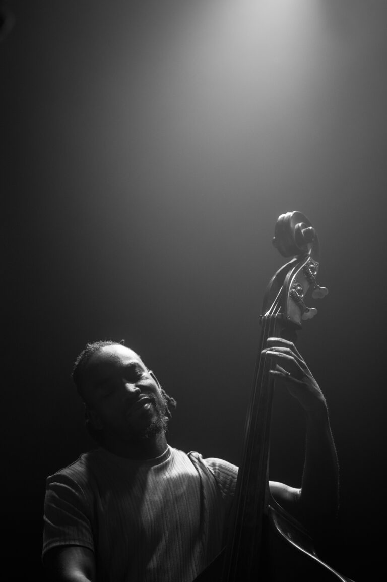 Een muzikant speelt een contrabas in een sfeervolle, lichtdoorlatende omgeving.
