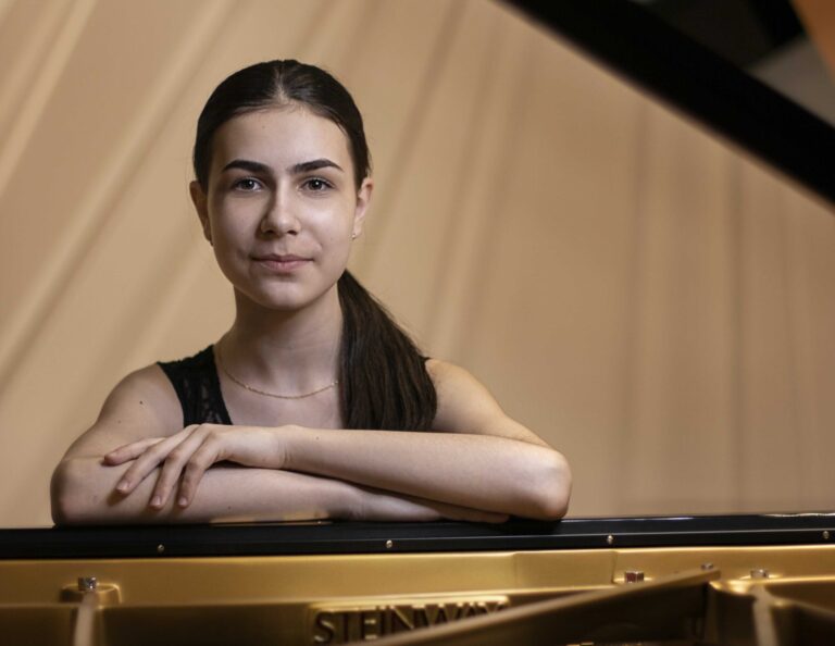 Alexandra achter de vleugel, haar armen geleund op het instrument