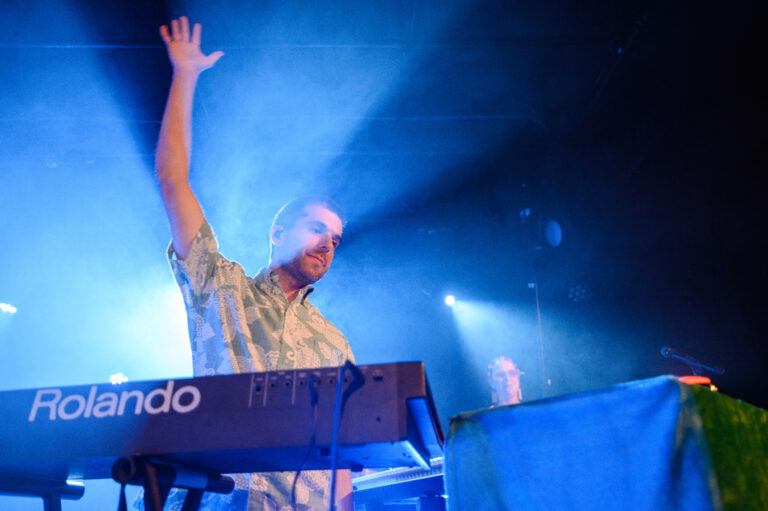 Een muzikant speelt enthousiast op een keyboard onder een blauwe lichtshow.