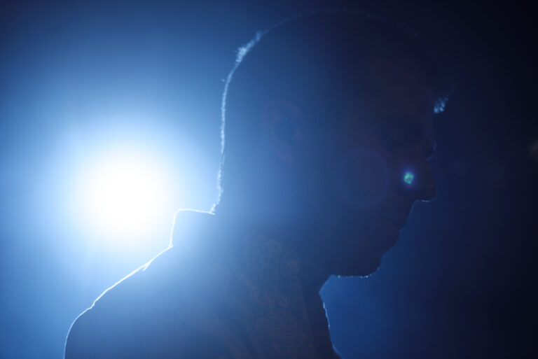 Silhouet van een persoon in profiel, verlicht door een opvallend blauwachtig licht op de achtergrond.