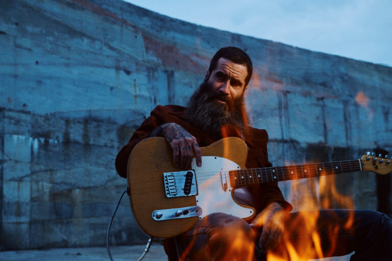 Man die net een gitaar voor een kampvuur zit.