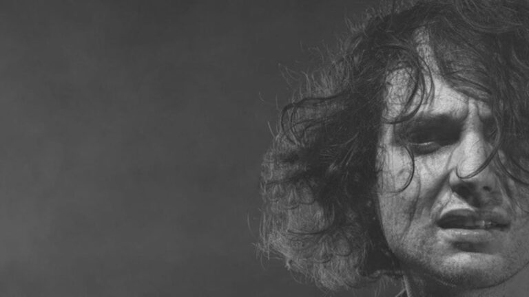 Zwart-wit portret van muzikant Dan Owen, met warrig haar en een intense gezichtsuitdrukking tegen een donkere achtergrond.