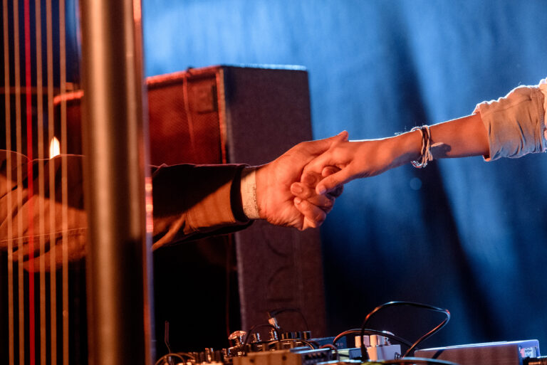 Twee handen pakken elkaar vast tegen een achtergrond van een podium.