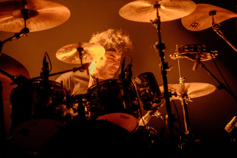 Een drummer die geconcentreerd speelt achter een set van verschillende percussie-instrumenten.